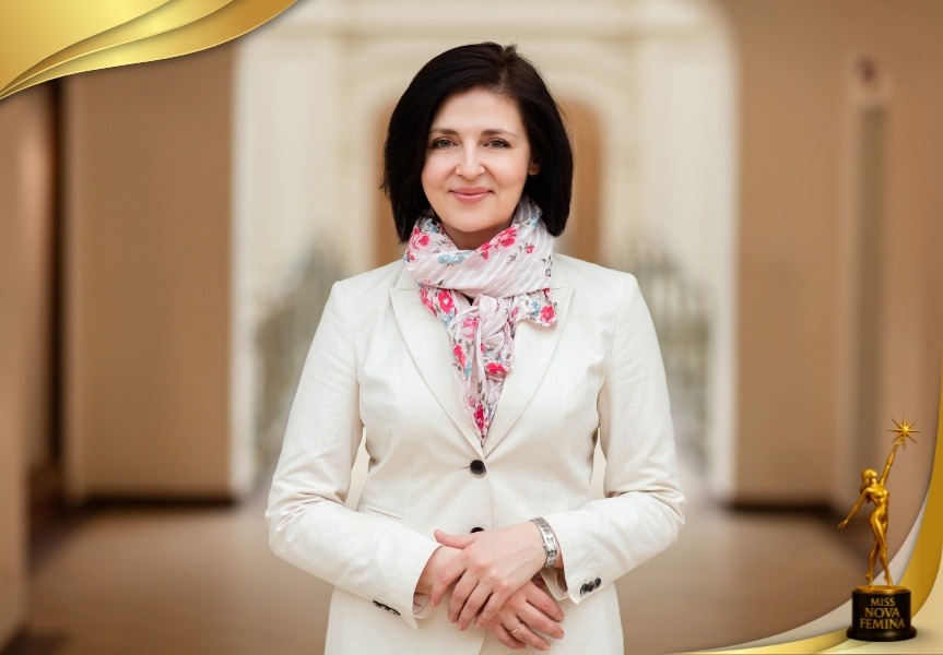 Mujer madura con traje blanco y bufanda floral, sonriendo con elegancia en Miss Nova Femina.