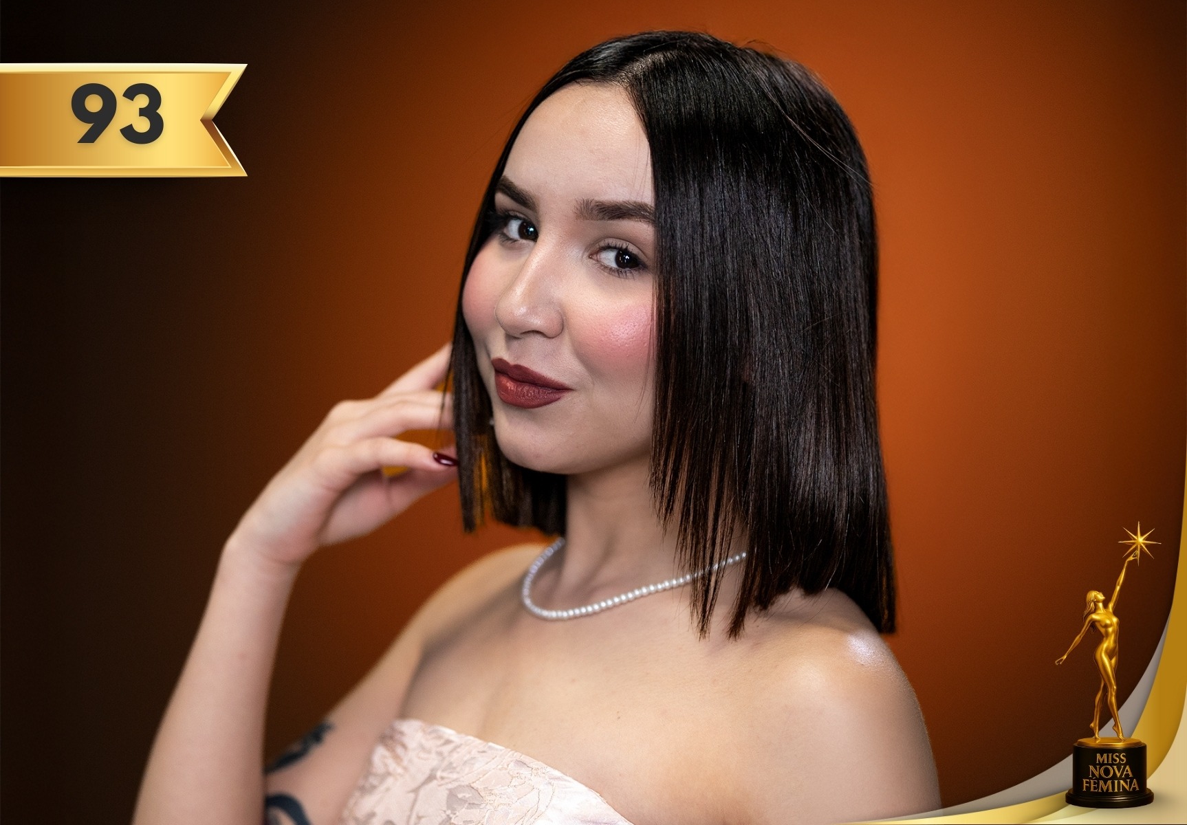 Lauren Dalila Rodríguez Marrero, concursante #93 de Miss Nova Fémina 2025, posando con un vestido claro y collar de perlas frente a un fondo naranja.
