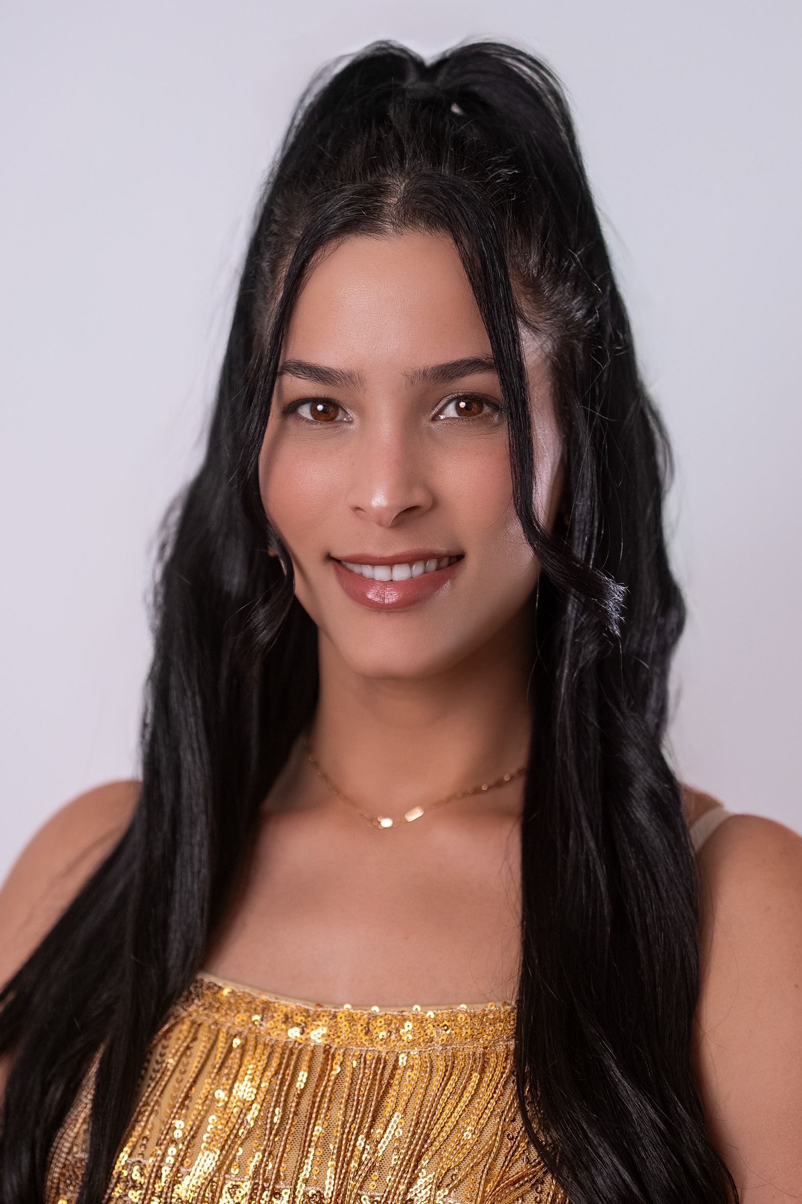 Retrato de Yaniuska Ávila González, concursante número 27 de Miss Nova Fémina, luciendo un vestido dorado elegante.