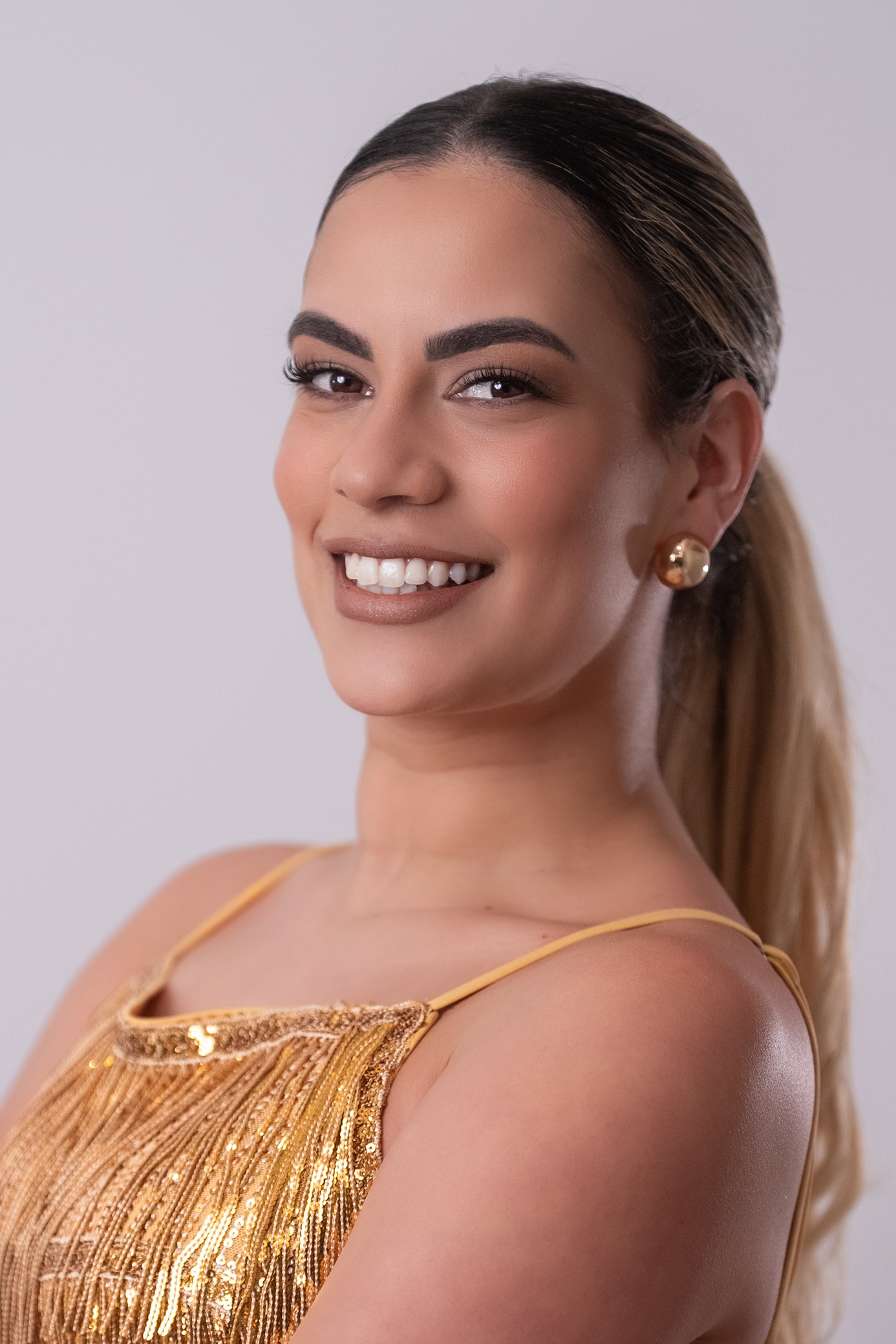 Retrato de Claudia Hernandez, concursante número 3 de Miss Nova Fémina, sonriendo con elegancia y luciendo un vestido dorado.